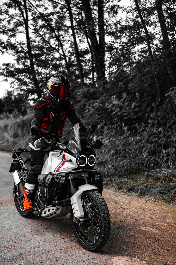 Motocyklista stojący na białym motocyklu adventure na leśnej drodze.