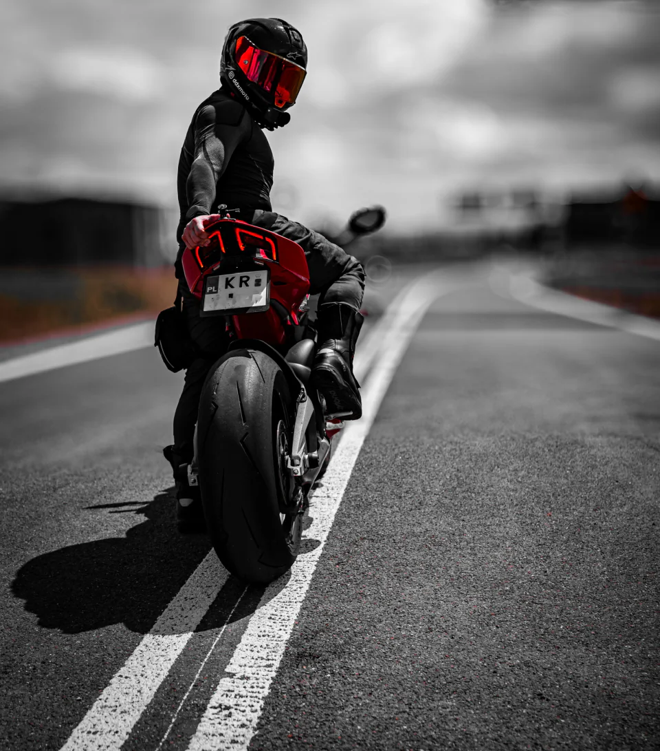Motocyklista siedzący na czerwonym motocyklu sportowym na otwartej drodze.